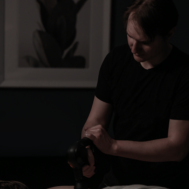 Andrew Radi using a theragun on a client at Vitality Massage Studio.
